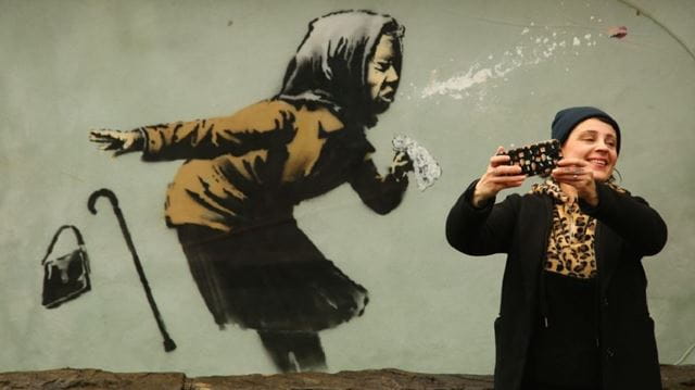 Socially distanced days out woman taking photo next to Banksy picture